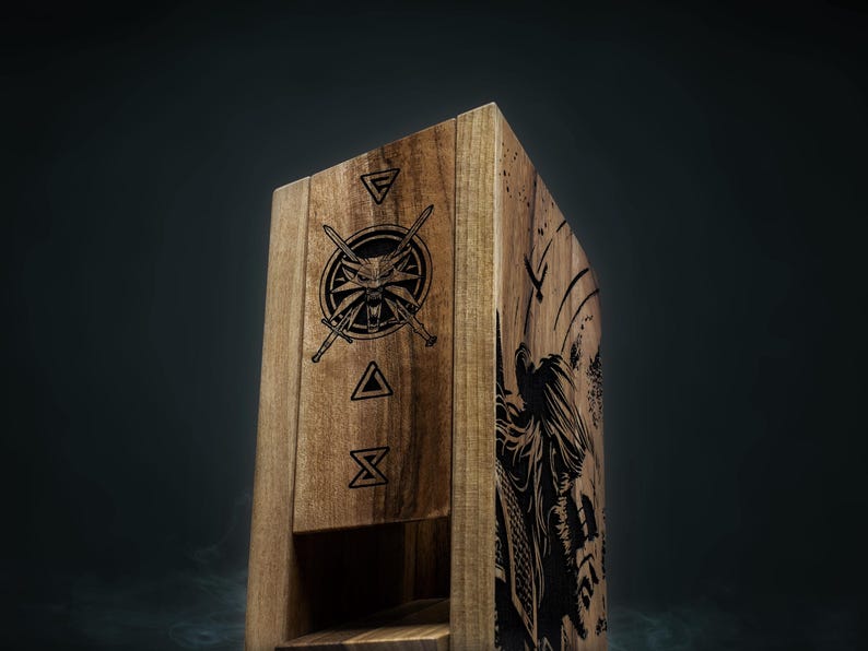 May include: Wooden box featuring engraved Witcher symbols and a detailed illustration of a figure. The box is made of light brown wood and has a hinged lid. The Witcher medallion and other symbols are etched on the front.