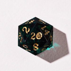 May include: A twenty-sided die with a dark green, marbled effect. The numbers are gold and the die is set against a white background. The die is a polyhedron, a geometric shape with multiple flat faces.