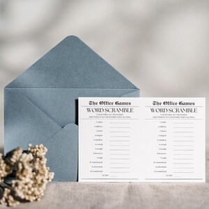 Op de afbeelding: Twee witte kaarten met zwarte tekst die "The Office Games Word Scramble" zegt en instructies om de woorden te ontcijferen. De kaarten liggen op een lichtblauwe envelop met een wit bloemenboeket.