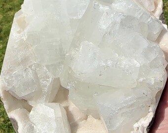 May include: A large, raw aquamarine crystal cluster. The crystal is a pale, translucent blue-green color with a rough, textured surface. The cluster is set against a light-colored matrix.