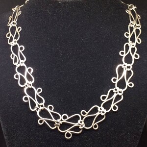 May include: A silver necklace with a delicate, intricate design. The necklace is made of multiple interconnected loops, creating a flowing, organic pattern.