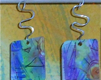 May include: A pair of earrings with abstract watercolor-style designs on rectangular shapes. The earrings are suspended from silver-toned, wavy wire.