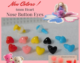 Op de afbeelding: Assortiment van 6 mm hartvormige plastic neusknopen in verschillende kleuren, waaronder rood, roze, geel, zwart en blauw. De ogen worden getoond naast een liniaal die 6 mm meet. De afbeelding bevat ook een kleine gehaakte engelpop en twee gehaakte teddyberen.