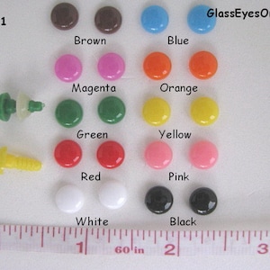 K&ouml;nnte beinhalten: Sortiment von 8 mm gro&szlig;en Sicherheitsaugen aus Kunststoff in verschiedenen Farben, darunter Braun, Blau, Magenta, Orange, Gr&uuml;n, Gelb, Rot, Rosa, Wei&szlig; und Schwarz. Die Augen sind paarweise auf einer wei&szlig;en Oberfl&auml;che mit einem Lineal zur Skalierung angeordnet. #RBE-1 GlassEyesOnline