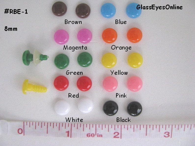 K&ouml;nnte beinhalten: Sortiment von 8 mm gro&szlig;en Sicherheitsaugen aus Kunststoff in verschiedenen Farben, darunter Braun, Blau, Magenta, Orange, Gr&uuml;n, Gelb, Rot, Rosa, Wei&szlig; und Schwarz. Die Augen sind paarweise auf einer wei&szlig;en Oberfl&auml;che mit einem Lineal zur Skalierung angeordnet. #RBE-1 GlassEyesOnline