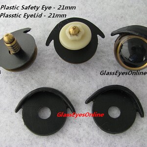 May include: Four plastic safety eyes and eyelids for crafts. The eyes are black with a gold rim and the eyelids are black. The eyes and eyelids are 21mm in diameter. The text #PE-1 Plastic Safety Eye - 21mm and #EL-1 Plasstic Eyelid - 21mm is visible in the image. The text GlassEyesOnline is visible in the image.