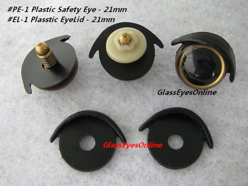 May include: Four plastic safety eyes and eyelids for crafts. The eyes are black with a gold rim and the eyelids are black. The eyes and eyelids are 21mm in diameter. The text #PE-1 Plastic Safety Eye - 21mm and #EL-1 Plasstic Eyelid - 21mm is visible in the image. The text GlassEyesOnline is visible in the image.