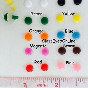 K&ouml;nnte beinhalten: Sortiment von 6 mm gro&szlig;en Kunststoffaugen in verschiedenen Farben, darunter Wei&szlig;, Schwarz, Gr&uuml;n, Gelb, Orange, Blau, Magenta, Braun, Rot und Pink. Die Augen sind nach Farben in Reihen angeordnet. Ein Lineal ist als Gr&ouml;&szlig;enreferenz enthalten. Das Lineal zeigt "60 in" und "RBE-1, 6mm".