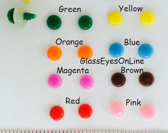 Op de afbeelding: Assortiment van 6 mm plastic ogen in verschillende kleuren, waaronder wit, zwart, groen, geel, oranje, blauw, magenta, bruin, rood en roze. De ogen zijn gerangschikt in rijen per kleur. Een liniaal is inbegrepen als referentie voor de grootte. De liniaal geeft "60 in" en "RBE-1, 6mm" aan.