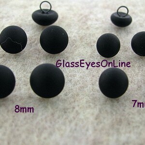 May include: Black plastic buttons with a shank, in two sizes: 7mm and 8mm. The buttons are shown on a light gray surface.