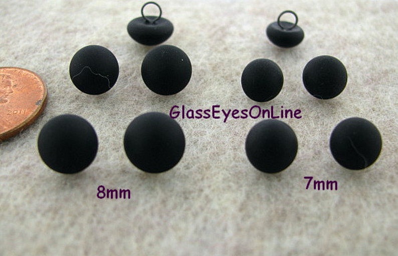 May include: Black plastic buttons with a shank, in two sizes: 7mm and 8mm. The buttons are shown on a light gray surface.