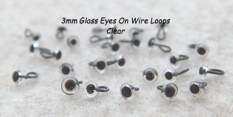 May include: A close-up of 3mm clear glass eyes on wire loops. The eyes are scattered on a white surface.