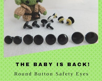 May include: A close-up of black plastic safety eyes for crafts. The eyes are round and have a shiny finish. The text "THE BABY IS BACK! Round Button Safety Eyes GLASSEYSONLINE.COM" is visible in the image.