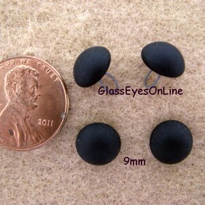 May include: Four black plastic buttons with a 9mm diameter. The buttons are shown next to a US penny for size comparison.  GlassEyesOnLine is printed on the image.