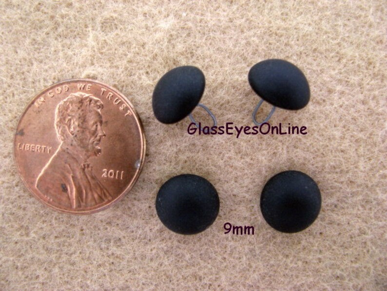 May include: Four black plastic buttons with a 9mm diameter. The buttons are shown next to a US penny for size comparison.  GlassEyesOnLine is printed on the image.