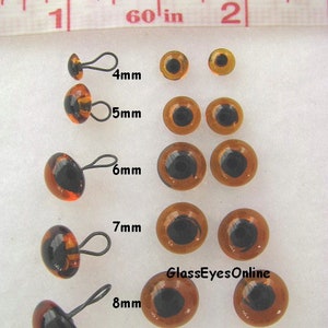 May include: Assortment of dark amber glass eyes with loops for crafts. The eyes range in size from 4mm to 8mm.  #LP201 - Glass Eyes with Loops - Dark Amber