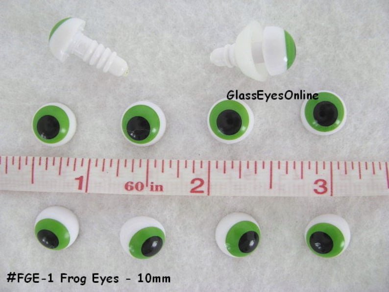 May include: A set of ten 10mm green plastic frog eyes with black pupils. The eyes are on a white surface with a ruler for scale. The text #FGE-1 Frog Eyes - 10mm is visible at the bottom of the image.
