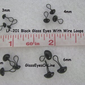 May include: Black glass eyes with wire loops in various sizes, 3mm, 4mm, 5mm, and 6mm. The eyes are shown next to a ruler for size reference. The text "LP-201 Black Glass Eyes With Wire Loops" and "GlassEyesOnLine" are also visible in the image.