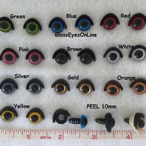 May include: Assortment of 10mm plastic safety eyes in various colors, including green, blue, red, pink, brown, white, silver, gold, orange, and yellow. The eyes are arranged in rows on a white surface with a ruler for scale. The text "GlassEyesOnLine" and "PEEL 10mm" are visible in the image.