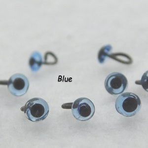 May include: Blue plastic safety eyes with black pupils and metal loop or screw backs. The eyes are arranged on a white surface. The text "Blue" is printed on the surface.