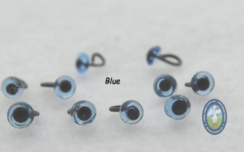 May include: Blue plastic safety eyes with black pupils and metal loop or screw backs. The eyes are arranged on a white surface. The text "Blue" is printed on the surface.