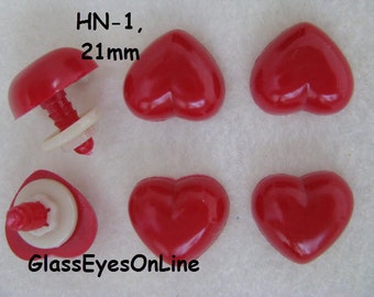 Può includere: Cinque occhi di sicurezza in plastica rossa a forma di cuore, ognuno con un diametro di 21 mm. Gli occhi hanno un retro in plastica nera e una rondella in plastica bianca. Il testo "HN-1, 21mm" è stampato sullo sfondo bianco.