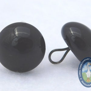 May include: Two black plastic safety eyes with a black plastic loop on one eye. The eyes are approximately 1 inch in diameter.