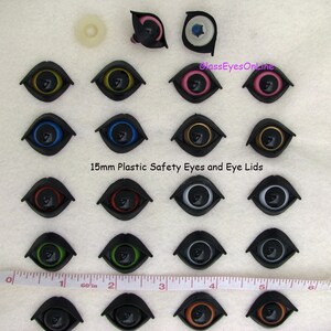 Puede incluir: Surtido de ojos de seguridad de pl&aacute;stico de 15 mm y p&aacute;rpados en varios colores, incluidos negro, blanco, azul, verde, rojo, dorado y marr&oacute;n. Los ojos est&aacute;n dispuestos en filas sobre una superficie blanca con una regla para la escala.
