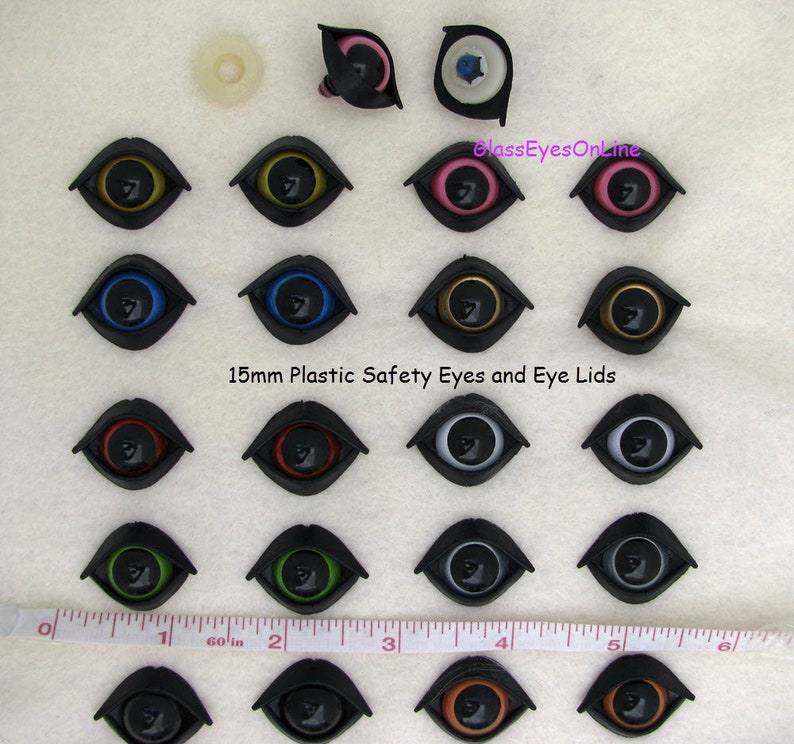 Puede incluir: Surtido de ojos de seguridad de pl&aacute;stico de 15 mm y p&aacute;rpados en varios colores, incluidos negro, blanco, azul, verde, rojo, dorado y marr&oacute;n. Los ojos est&aacute;n dispuestos en filas sobre una superficie blanca con una regla para la escala.