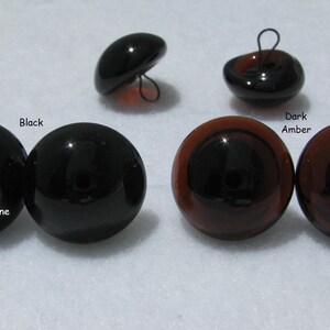 May include: Four pairs of glass eyes for crafts. Two black eyes, two dark amber eyes. The eyes are round and have a black pupil.