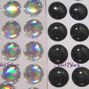 May include: Two sheets of adhesive backed, round, self-adhesive stickers. One sheet has 12 iridescent silver stickers. The other sheet has 12 black stickers. The text "Solid Silver" is printed below the silver stickers. The text "Solid Black" is printed below the black stickers.