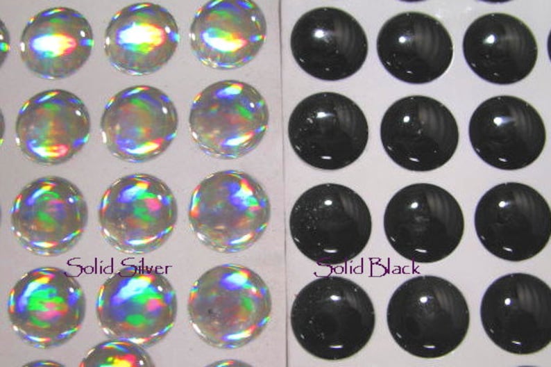May include: Two sheets of adhesive backed, round, self-adhesive stickers. One sheet has 12 iridescent silver stickers. The other sheet has 12 black stickers. The text "Solid Silver" is printed below the silver stickers. The text "Solid Black" is printed below the black stickers.