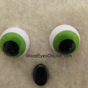 May include: Two large, round, plastic googly eyes with white pupils and green irises. The eyes are on a light brown, fuzzy surface.