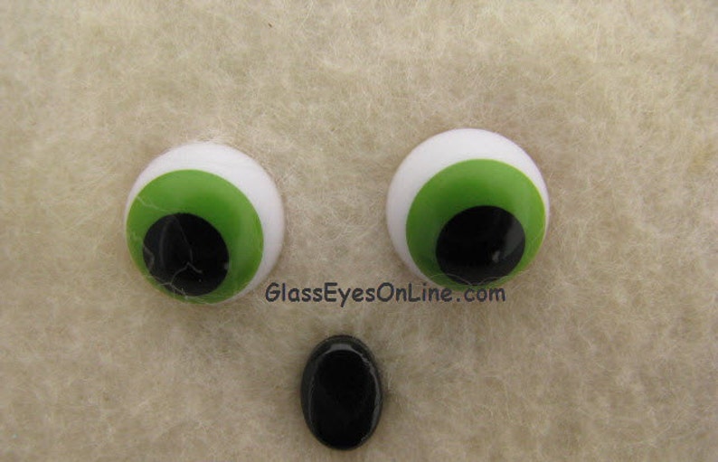 May include: Two large, round, plastic googly eyes with white pupils and green irises. The eyes are on a light brown, fuzzy surface.