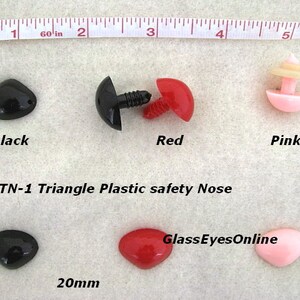 Pode incluir: Tr&ecirc;s narizes de seguran&ccedil;a de pl&aacute;stico em forma triangular em preto, vermelho e rosa. Os narizes medem 20 mm e s&atilde;o mostrados em uma superf&iacute;cie branca com uma r&eacute;gua para escala. O texto '#TN-1 Triangle Plastic safety Nose' e 'GlassEyesOnline' tamb&eacute;m s&atilde;o vis&iacute;veis na imagem.
