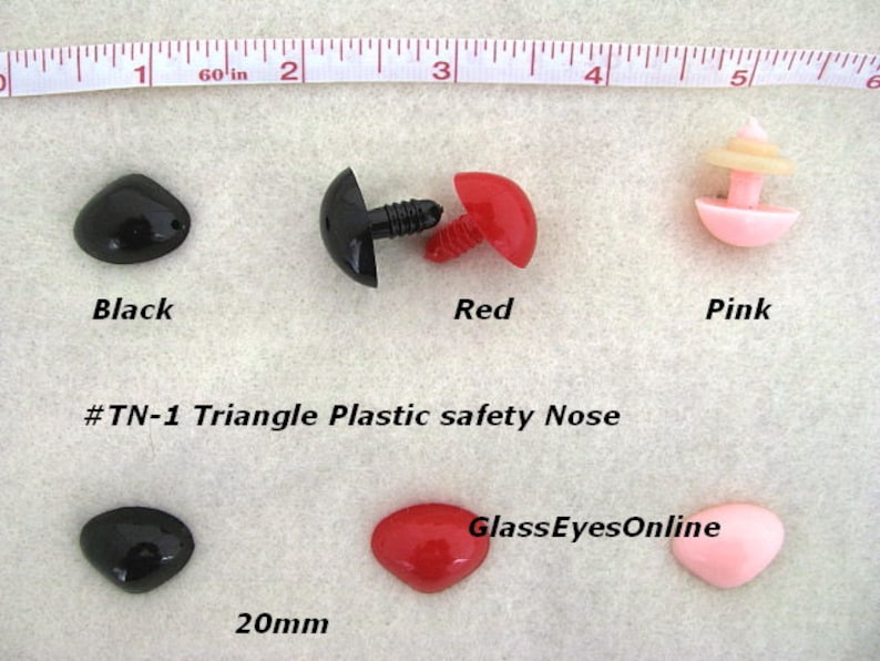 Pode incluir: Tr&ecirc;s narizes de seguran&ccedil;a de pl&aacute;stico em forma triangular em preto, vermelho e rosa. Os narizes medem 20 mm e s&atilde;o mostrados em uma superf&iacute;cie branca com uma r&eacute;gua para escala. O texto '#TN-1 Triangle Plastic safety Nose' e 'GlassEyesOnline' tamb&eacute;m s&atilde;o vis&iacute;veis na imagem.