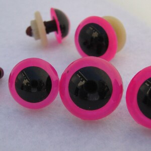 May include: Six pink and black plastic safety eyes with a black pupil and a pink outer ring. The eyes have a white plastic washer and a black plastic post.