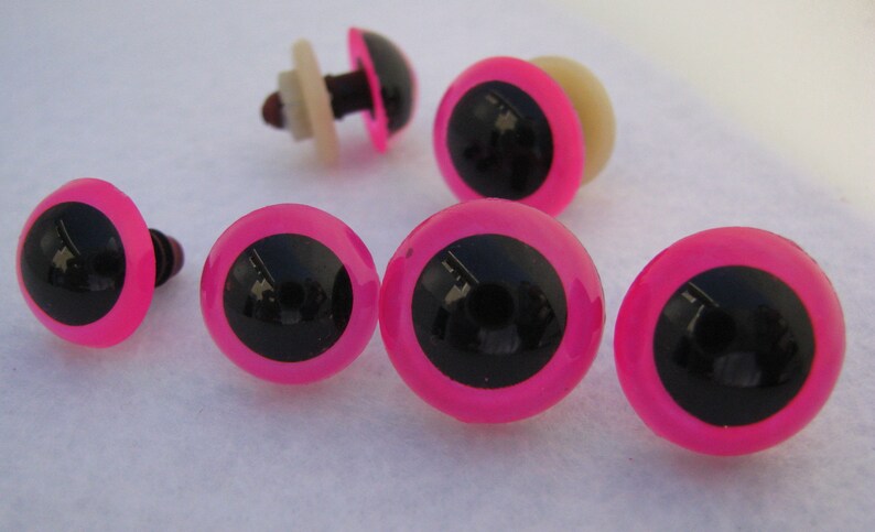 May include: Six pink and black plastic safety eyes with a black pupil and a pink outer ring. The eyes have a white plastic washer and a black plastic post.
