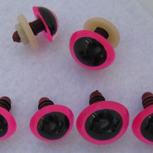 May include: Eight pink plastic safety eyes with black pupils and a brown screw back. The eyes are approximately 1 inch in diameter.