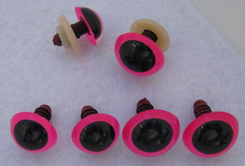 May include: Eight pink plastic safety eyes with black pupils and a brown screw back. The eyes are approximately 1 inch in diameter.