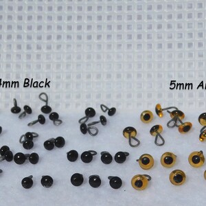 May include: A close-up of two sets of plastic safety eyes for crafts. The set on the left is 4mm black eyes and the set on the right is 5mm amber eyes.