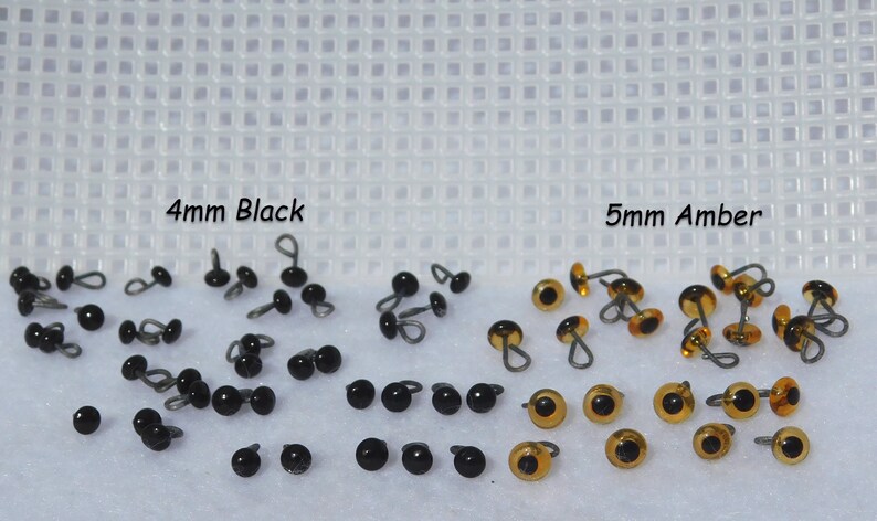 May include: A close-up of two sets of plastic safety eyes for crafts. The set on the left is 4mm black eyes and the set on the right is 5mm amber eyes.