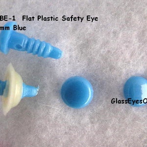 K&ouml;nnte beinhalten: Vier blaue Sicherheitsaugen aus Kunststoff, zwei mit einer wei&szlig;en Kunststoffr&uuml;ckseite und zwei flache, runde Augen. Die Augen haben einen Durchmesser von 6 mm. Der Text "RBE-1 Flat Plastic Safety Eye 6mm Blue" ist oben im Bild sichtbar. Der Text "GlassEyesOnline" ist unten im Bild sichtbar.