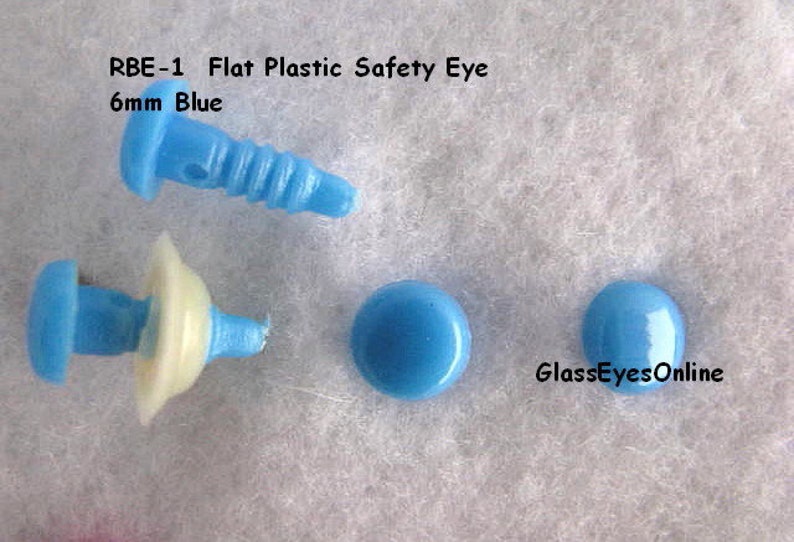 K&ouml;nnte beinhalten: Vier blaue Sicherheitsaugen aus Kunststoff, zwei mit einer wei&szlig;en Kunststoffr&uuml;ckseite und zwei flache, runde Augen. Die Augen haben einen Durchmesser von 6 mm. Der Text "RBE-1 Flat Plastic Safety Eye 6mm Blue" ist oben im Bild sichtbar. Der Text "GlassEyesOnline" ist unten im Bild sichtbar.
