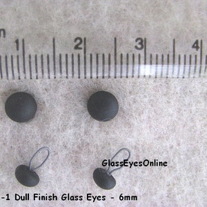 Op de afbeelding: Vier zwarte glazen ogen met een matte afwerking, met een diameter van 6 mm. Twee van de ogen hebben een zwarte lus om te naaien.