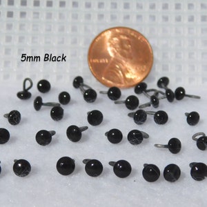 May include: A close-up of 5mm black plastic safety eyes with a metal loop for sewing. The eyes are shown next to a US penny for size comparison. 5mm Black.