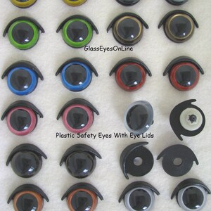 Puede incluir: Surtido de ojos de seguridad de pl&aacute;stico de 21 mm con p&aacute;rpados en varios colores, incluyendo negro, marr&oacute;n, rojo, azul, verde y gris. Los ojos est&aacute;n dispuestos en filas sobre una superficie blanca con una regla para la escala. El texto "GlassEyesOnLine" y "Plastic Safety Eyes With Eye Lids" es visible en la imagen.