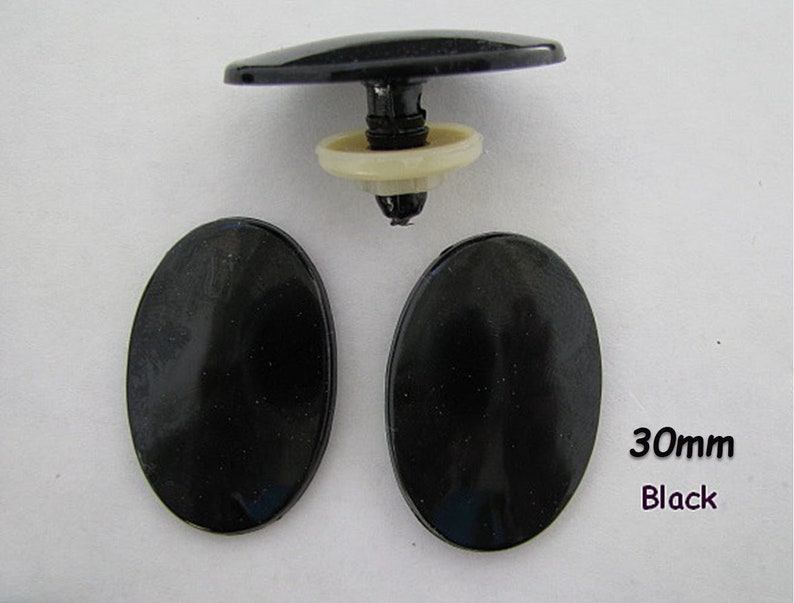 May include: Three black plastic oval-shaped buttons, each measuring 30mm in diameter. The buttons have a smooth, glossy finish. The text "30mm Black" is visible in the lower right corner of the image.