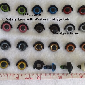 Puede incluir: Surtido de ojos de seguridad de pl&aacute;stico de 10 mm con arandelas y p&aacute;rpados en varios colores, incluidos verde, azul, rojo, rosa, marr&oacute;n, gris, dorado y negro. Los ojos est&aacute;n dispuestos en filas sobre una superficie blanca con una regla para la escala. El texto "PEEL 10mm" y "Plastic Safety Eyes with Washers and Eye Lids" es visible en la parte superior de la imagen. El texto "GlassEyesOnLine" es visible en la parte inferior de la imagen.