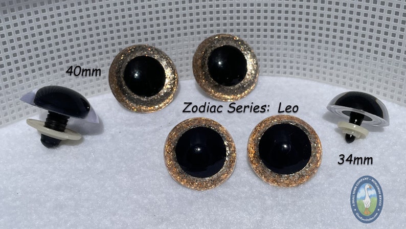 May include: Four black and gold glitter safety eyes for crafts. Two eyes are 40mm and two are 34mm. The eyes have a gold glitter rim and a black center. The text "Zodiac Series: Leo" is visible in the image.